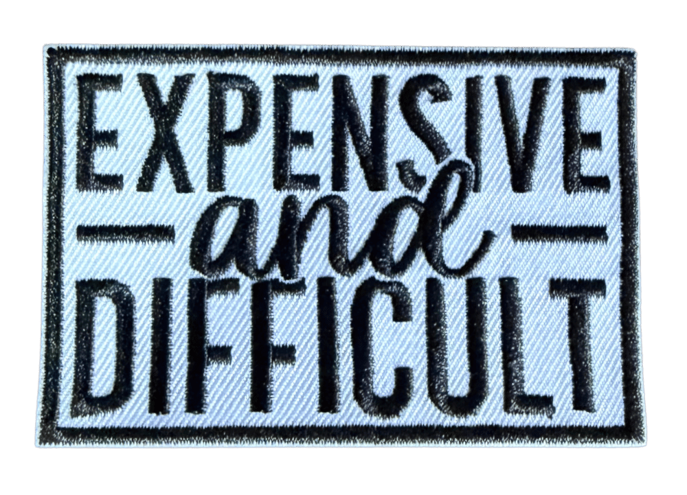Expensive and Difficult embroidered patch with white script lettering on dark background