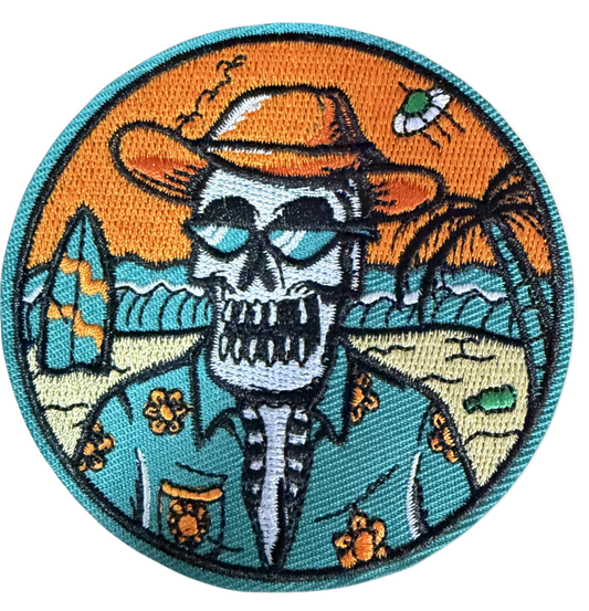 Circular patch with skull in cowboy hat at beach with surfboards and palm trees at sunset