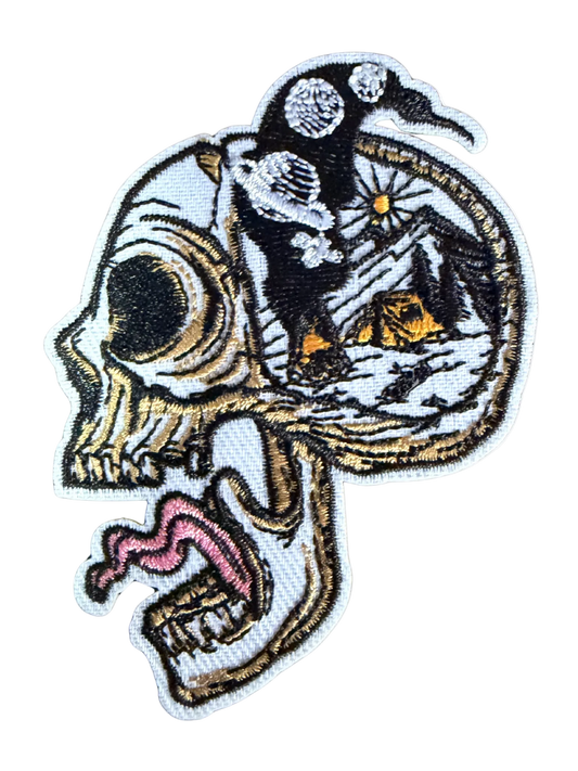 Skull side profile with open cranium showing mountain camping scene under starry night sky patch