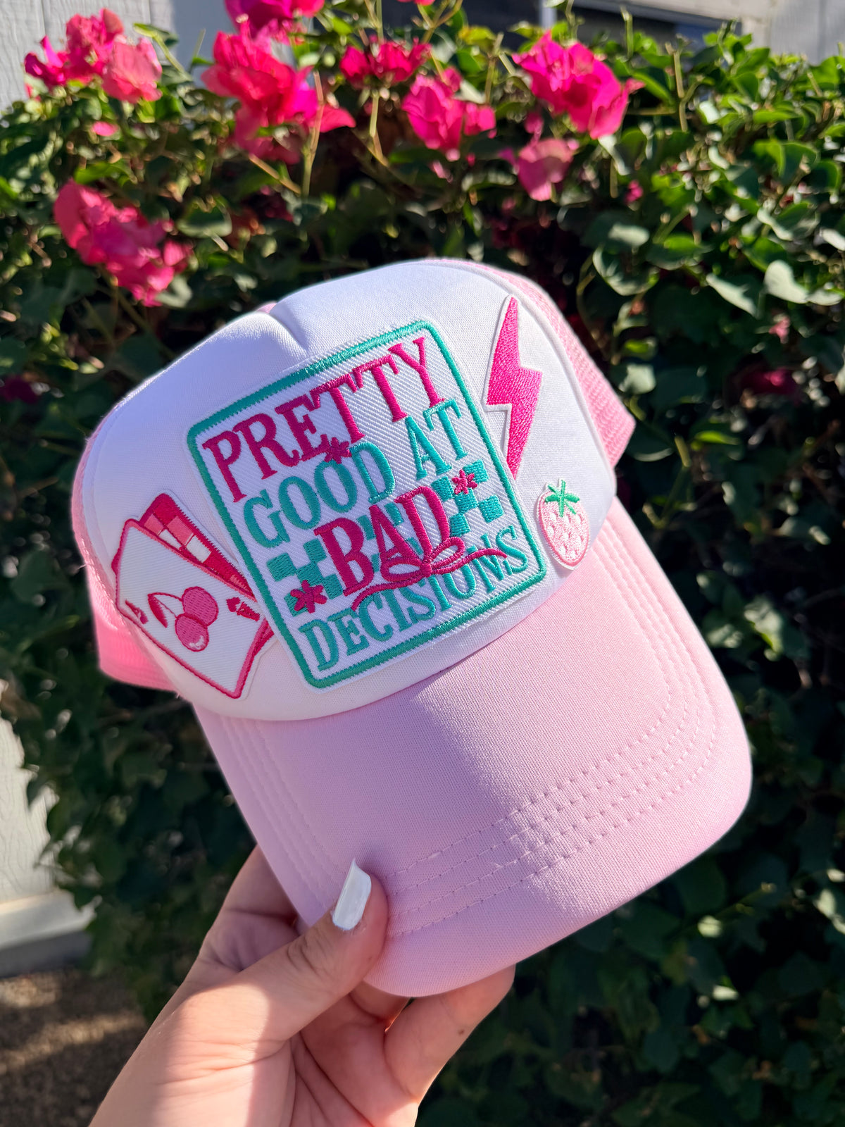 Pink cap with text and graphics held by a hand against a floral background